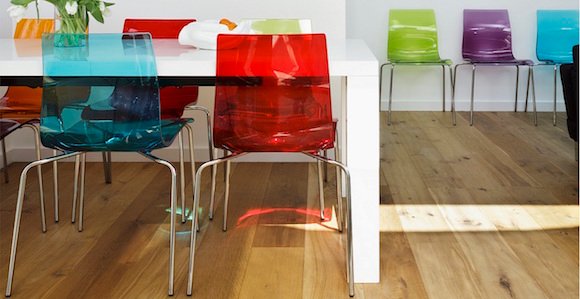 Colourful plastic chairs at white dining table opposite modern artworks on wall